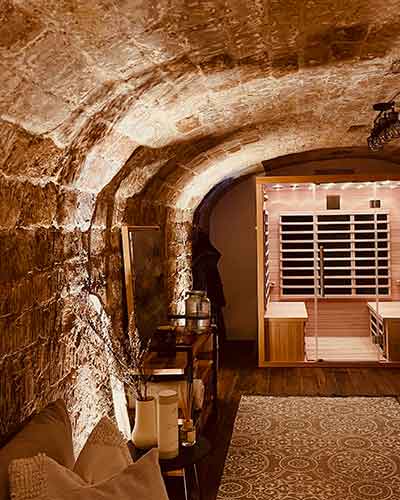 Cave voutée transformée en espace détente avec spa, parquet bois foncé, canapé et lumières tamisées.