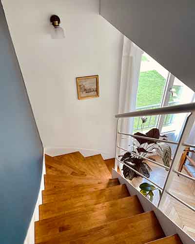 Escalier rénové avec marches en bois clair, murs bicolores blancs et gris bleu, vue sur salon lumineux.
