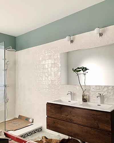 Salle de bain rénovée avec douche à l’italienne, double vasque en bois foncé et carrelage blanc.